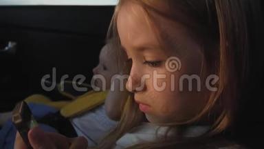可爱的小女孩坐在汽车座位上玩智能手机。